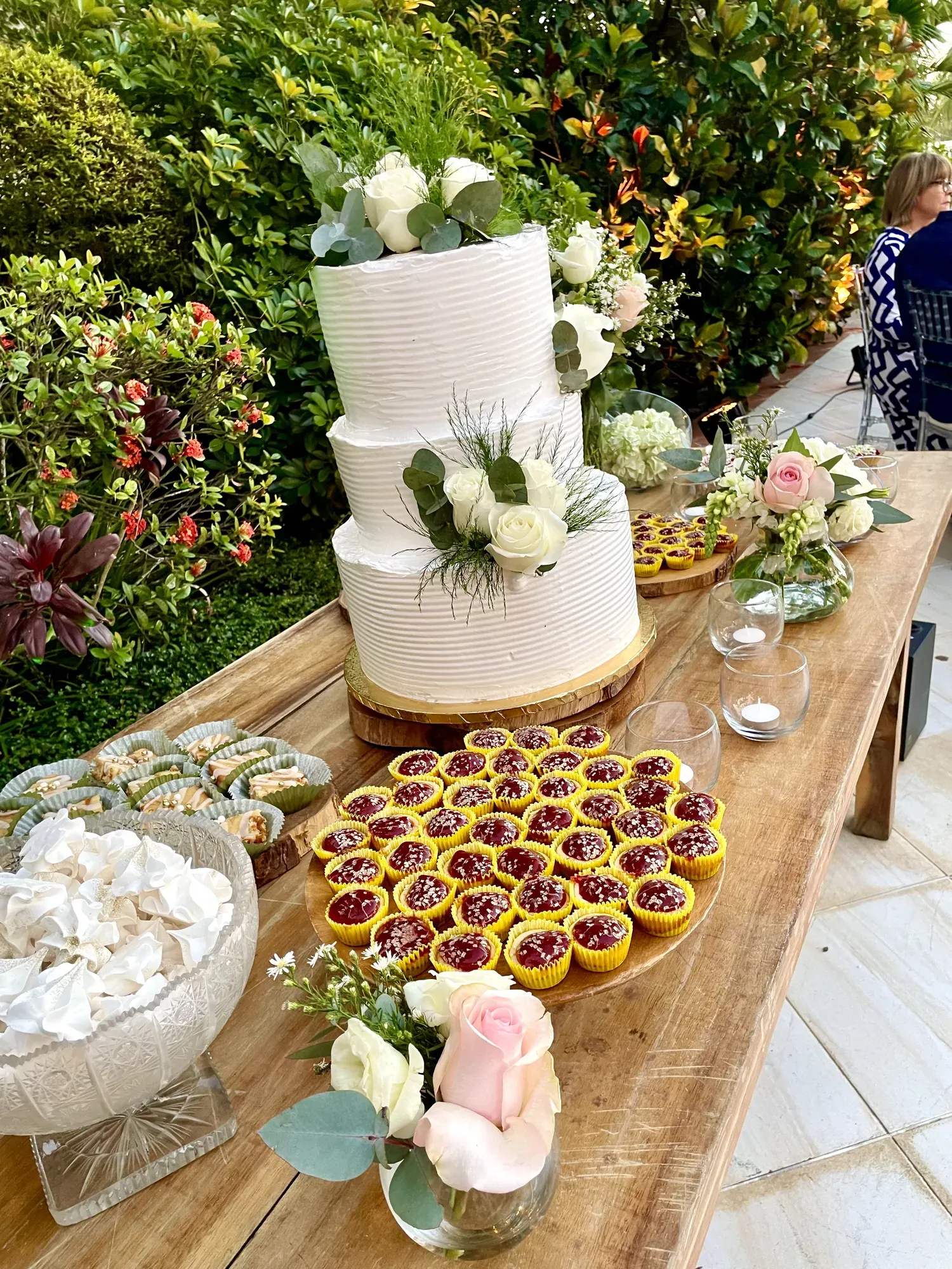 Bizcocho blanco de tres pisos junto a una mesa de postres en un jardín