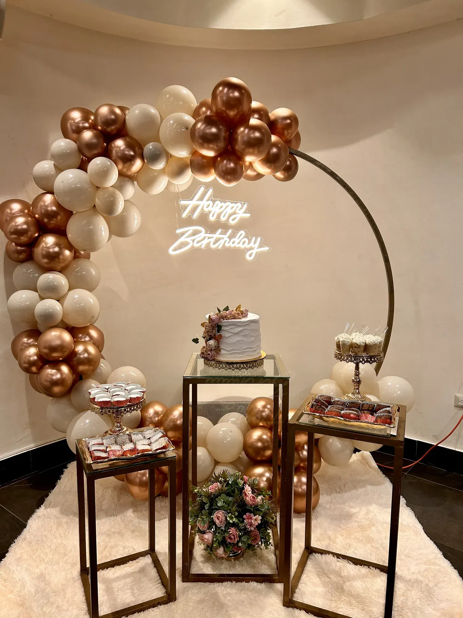 Arco de globos dorados con pedestales y letrero de cumpleaños