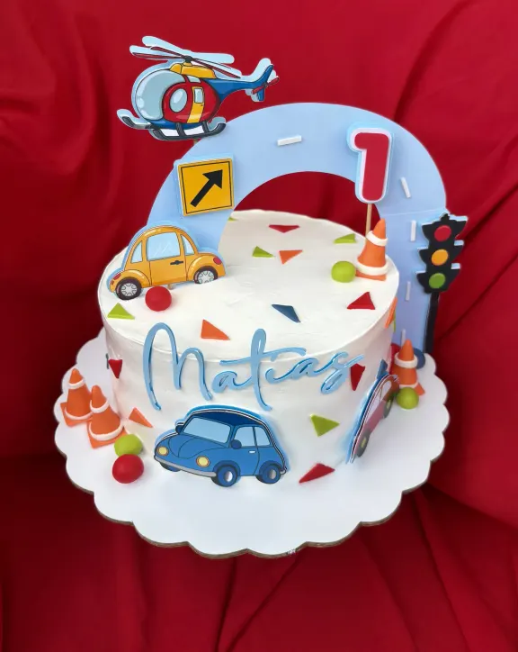 Bizcocho blanco con topper de carritos y señales de tránsito para un primer cumpleaños