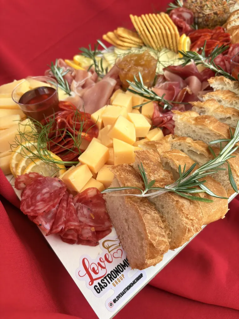 Tabla de charcutería con quesos, embutidos y pan sobre mantel rojo